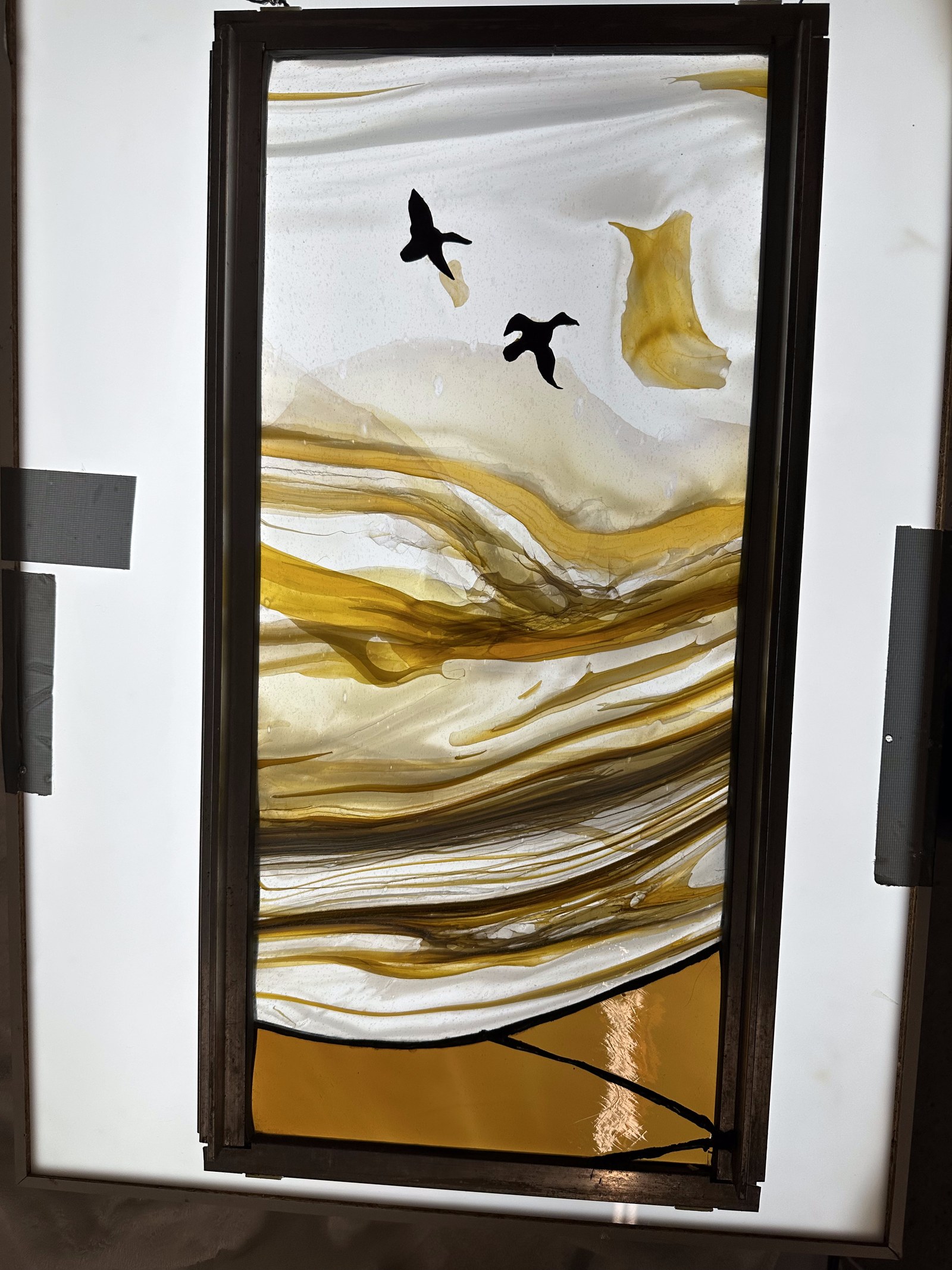 Amber streaky glass panel with birds in flight, on a lightbox