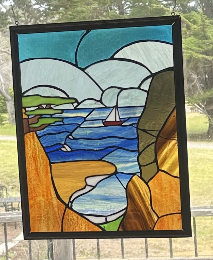 Stained glass panel of a coastal cliff and sailboat