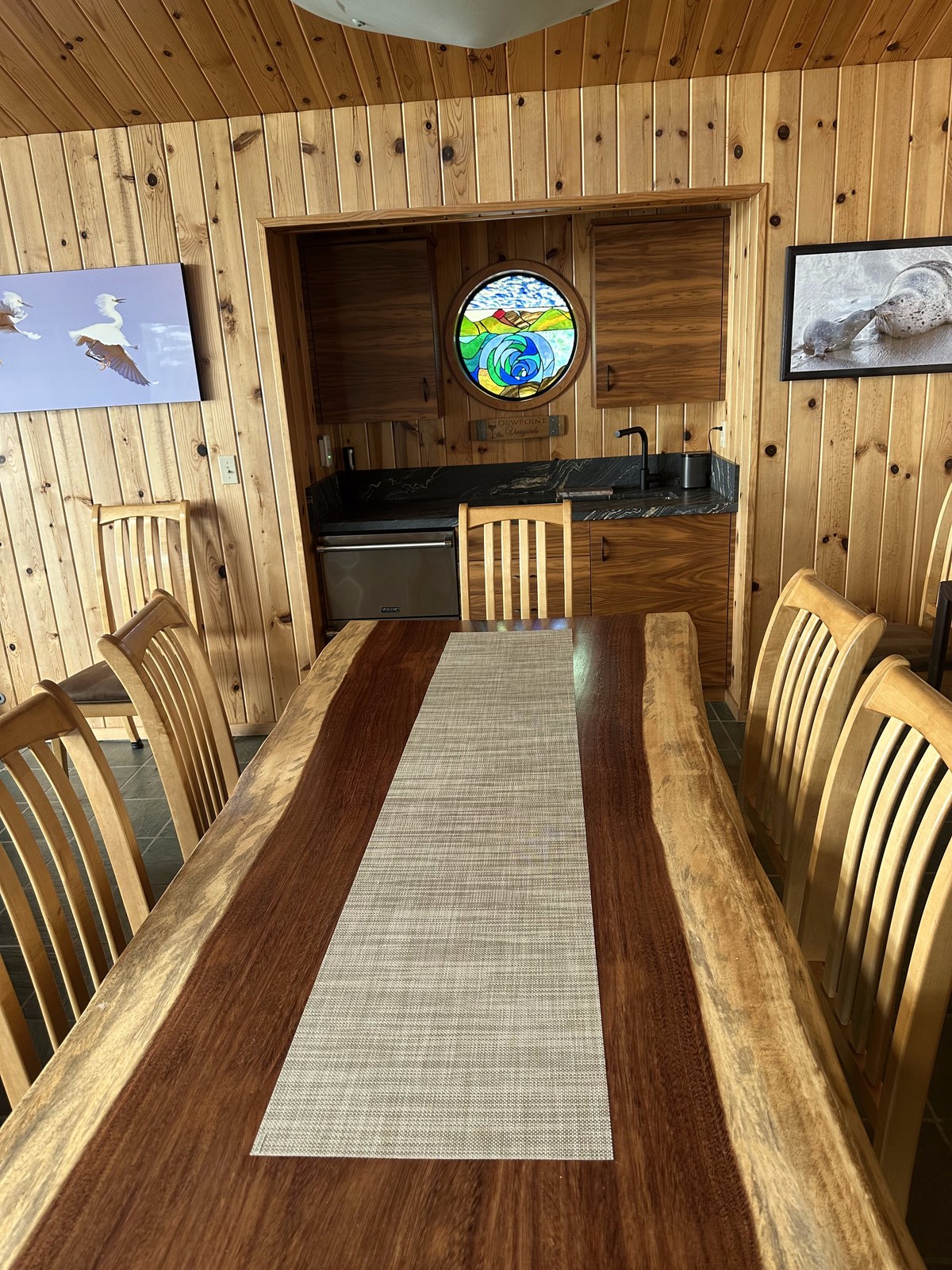 Dining table with the round DewPoint Vineyards window in the wet bar beyond